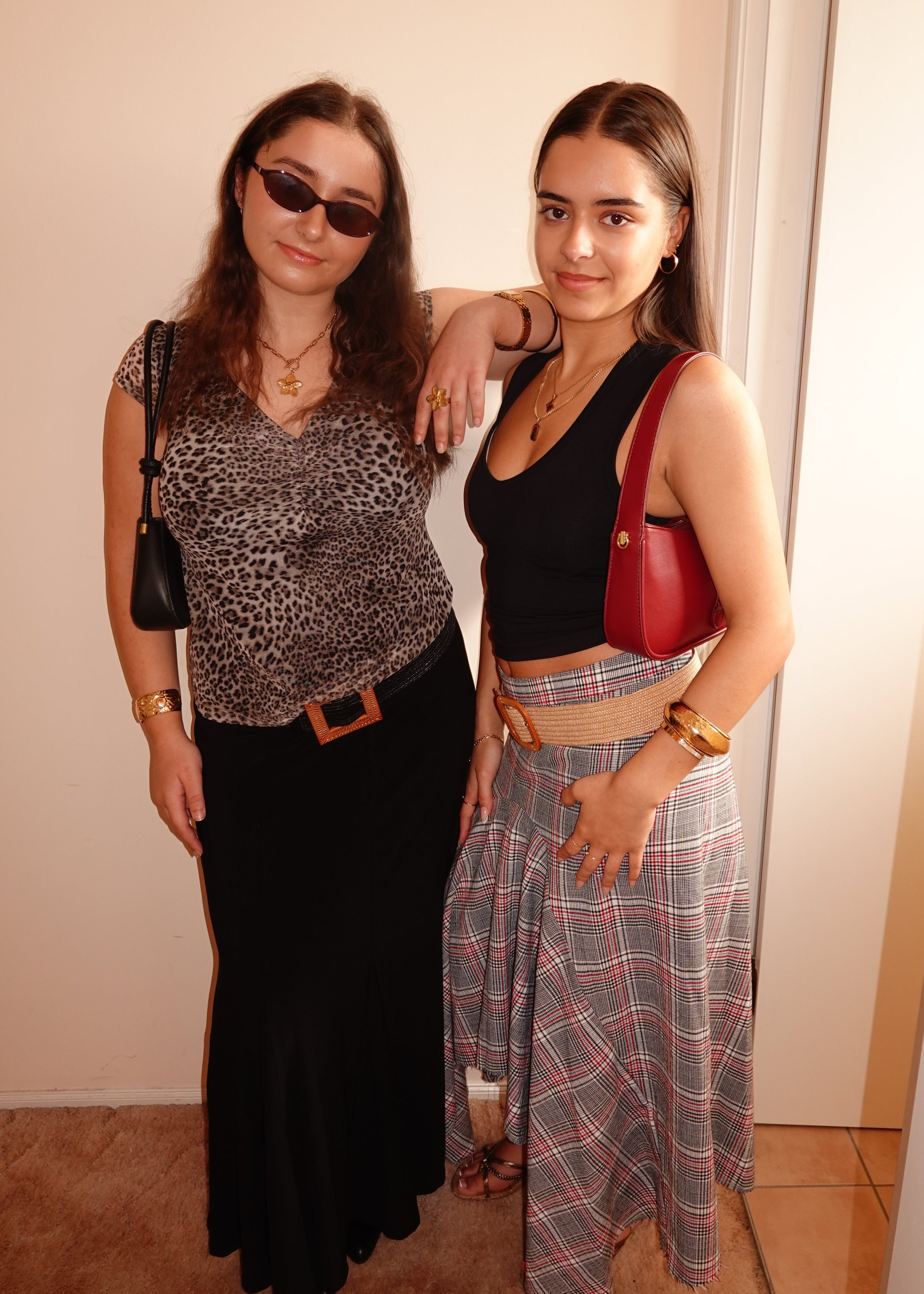 Two women standing together indoors, one wearing sunglasses and a leopard print top, the other in a black top and plaid skirt.
